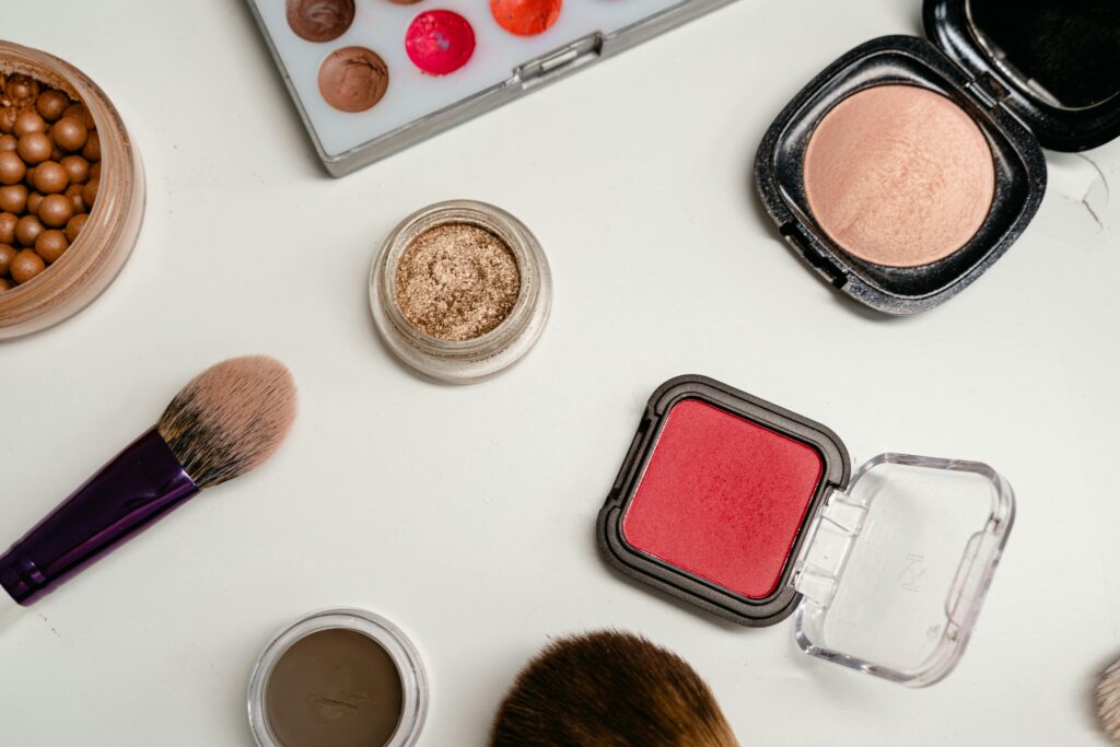 Flat lay of various makeup products including brushes, powders, and creams on a white surface.