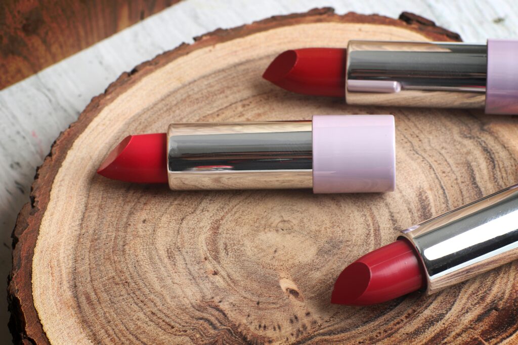 Close-up of red lipsticks arranged on a wooden tray, showcasing beauty products in a rustic setting.